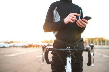 Bir adam bir bisiklet ile bir akıllı telefon yardım Close-up. Bisiklet binici dinlenme ve bir smartphone kullanarak. Bisikletçi ile güneşin sokakta bir bisiklet ve bir akıllı telefon kullanır. Boşaltmak.