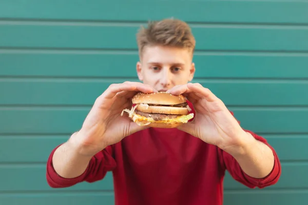 Young Man Stands Turquoise Background Holds Appetizing Burger His Hands — Stock Photo, Image