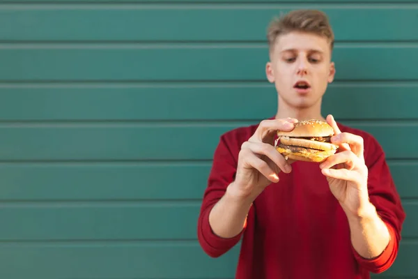 Gutaussehender Junger Mann Hält Einen Appetitlichen Burger Der Hand Und — Stockfoto