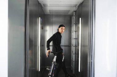 Asansörde bir bisiklet ile genç bir bisikletçi portresi. Genç bir adam bir bisiklet ile bir asansörde iner.