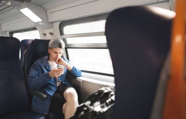 Bir treni pencerenin yakınında oturan, seyahat ve bir smartphone kullanarak odaklı bir adam portresi. Trende yolculuk.