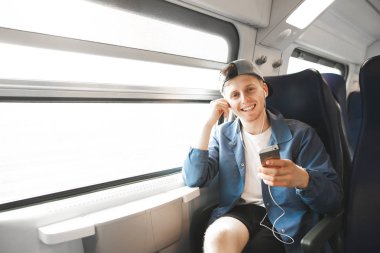 Pencerenin önüne bir tren sürme ve gülümseyerek kameraya bakarak gülümseyen bir genç adam onun elinde bir akıllı telefon ile portresi. Gülümseyen turistik bir gezi bir Internet bağlantısında sahiptir.