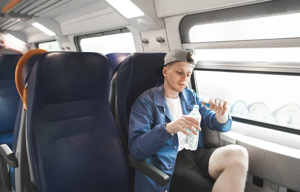 Nice guy trains a train. Portrait of a young man sitting in a train near the window and looking at the bottle in his hands.