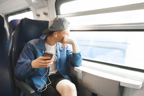 Молодой Человек Сидит Поезде Окна Смартфоном Руках Смотрит Окно Слушает — стоковое фото