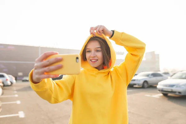 Uśmiechnięte Dziewczyny Żółtą Bluzę Kapturem Nabiera Żółte Przypadku Smartfon Autoportretów — Zdjęcie stockowe