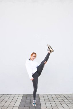 Spor kız beyaz bir duvar arka plan üzerinde duruyor ve Çalıştır önünde durulama. Spor giyim kadın germe ayakta yapar. Spor kavramı.