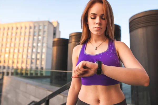 Sexy sports girl looks at her hand with a smart watch. Focus on hand with watch. Sports with smart watch. Sports concept.