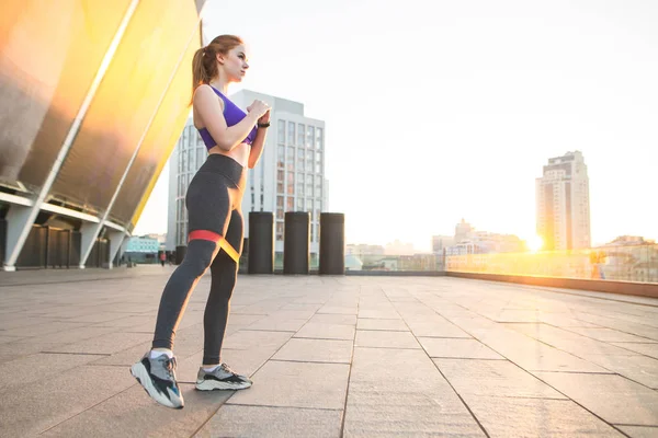 Street portrait of a sports girl in sportswear makes stretching and training against the background of the city in the east. Morning sports. Copyspace. Street fitness