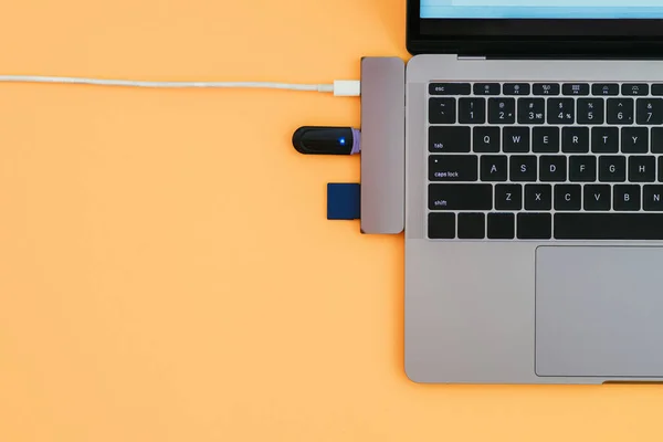 Modern laptop, USB Type-C adapter with a flash and charging on orange background. Technology concept. Copyspace. Adapter for new standards.