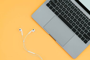 Modern güzel defter ve sarı bir arka plan, üstten görünüm üzerinde beyaz kulaklık. Müzik ile bir dizüstü bilgisayar üzerinde çalışmaya Flatlay.Copyspace..