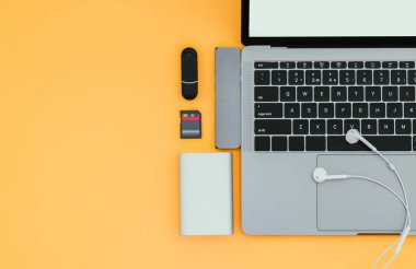 Bir sarı arka plan, üstten görünüm, işyeri dizüstü bilgisayar Usb türü-C adaptörü, flash sürücüler, kulaklık ve güç banka ile. Gadget'lar için modern bir dizüstü bilgisayarı kullanıyor. Teknoloji kavramı. Flatlay