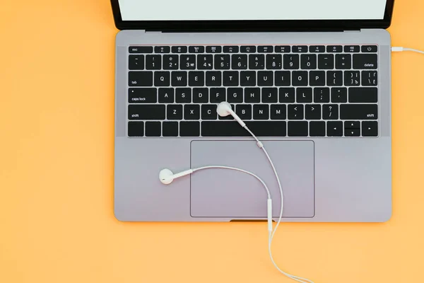 Modern metallic laptop and white headphones isolated on a yellow background and copyspace, top view. Flat lay . Work on a laptop with music.