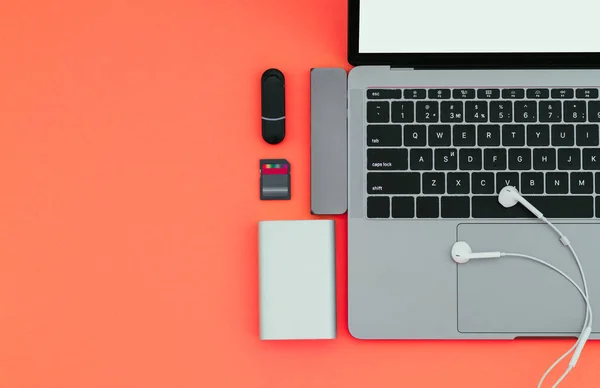 Laptop with USB Type-C adapter, flash drives, headphones and Power Bank on a red background, top view, workplace. Gadgets for use a modern laptop. Technology concept.