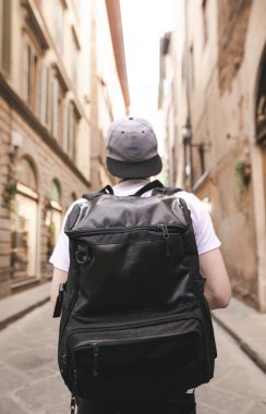 Bir turist ile büyük bir siyah sırt çantası portresi şehrin dar sokaklarında ve ileri görünüyor. Arkasında bir turist İtalya sokaklarında bir sırt çantası ile.