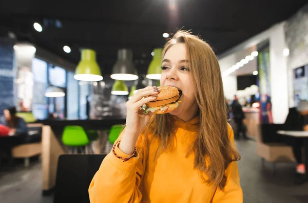 Porträtt Vacker Flicka Orange Hoodie Biter Aptitretande Burgare Mot Bakgrund — Stockfoto