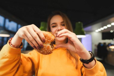 Turuncu giyim çekici kız harika lezzetli hamburger elinde tutan ve kalp belirtisi gösterir. Kız hamburger sever. Lokanta için seviyorum. Boşaltmak