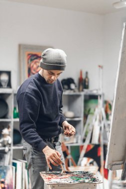 Portre rahat bir stüdyoda ayakta ve yağlı boya, karıştırma bir moda sanatçının boya bir resim. Portre ressam iş başında. Boyama kavramı.