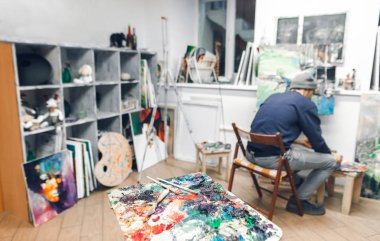 Yağlı boya ve fırça sanat stüdyosu ve sanatçı arka plan üzerine palet boya bir resim. Ressam ön planda bir sanat stüdyosu resimde Fırçalar paleti boyar..