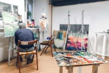 Palet ve fırça bir sandalyede oturan bir ressam arka plan üzerinde durmak ve boya bir resim Hostel rahat bir stüdyoda. Studio resim. Resim atölyesi