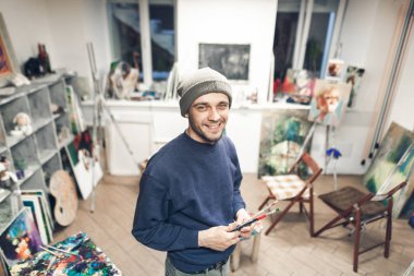 Sanat Okulu gülümseyen bir öğrenci portresi kameraya bakarak stüdyonun arka plan üzerinde duruyor. Resim sanat atölyesi arka plan üzerinde gülümseyen öğretmeni. Kendi stüdyosunda mutlu sanatçı.