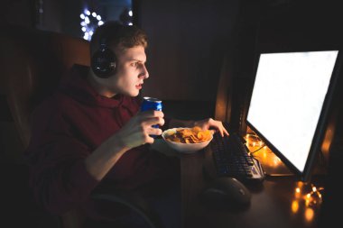 Ekrana bakarak bir bilgisayarda evde video oyunları oynamak ve kola, içme genç bir adam portresi. Cips ve cola gece bilgisayarda oyun yemekleri. Oyun ve hızlı gıda.