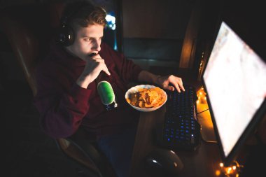 Bir pozitif oyun oyun oynarken cips ile bira içme bir bilgisayarda portresi. Mutlu adam evde, çalışma masası oturma ekrana, gülümseyerek ve bir şişe bira, çerez yemek tutan bakarak.