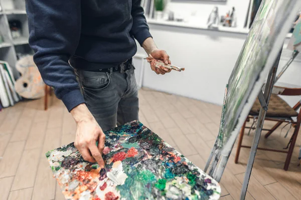 艺术家的手与画笔和调色板刀 画在画布上 混合在托盘上的油漆 画家在艺术工作室里画一幅画 用刷子把手放在手上 — 图库照片