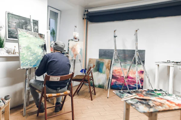 才华横溢的艺术家坐在舒适的艺术工作室的椅子上 画一幅油画 创意氛围 创意艺术家在工作室里创作绘画 — 图库照片