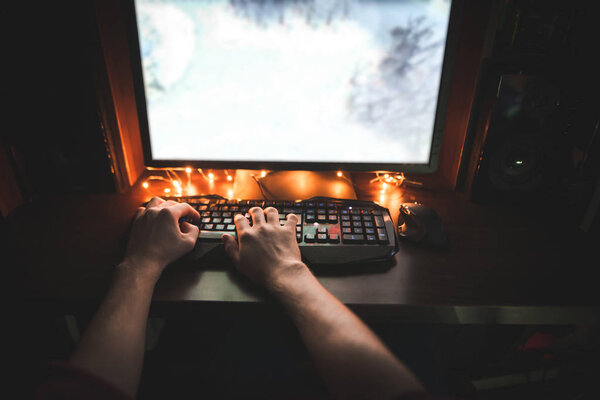 A man uses a computer at night. The first-person view, the man's hands on the mouse and the keyboard play games on the computer. Gamer plays games at night on the computer.