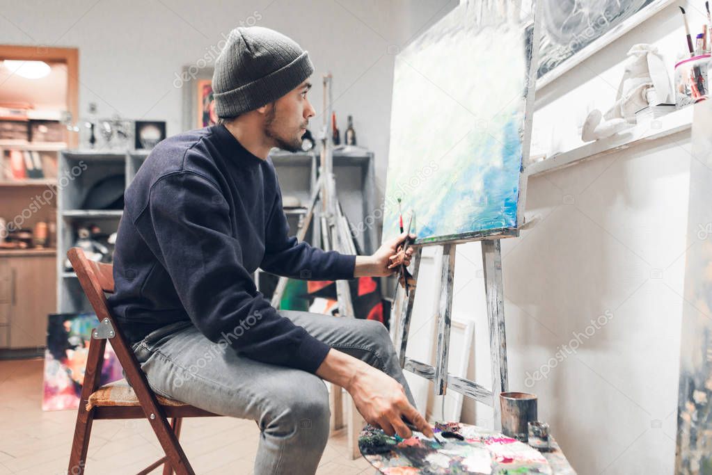 Portrait of an artist student sitting in class and painting a painting on canvas. Education at art school. Man learns painting.