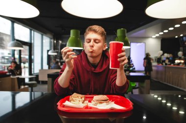 Genç bir adam portresi bir masada oturan bir restoranda fast food yiyor. Patates kızartması ve hamburger, bir içki onun elinde tutan tepsi. Öğrenci patates kızartması bir fast-food restoran yiyor..