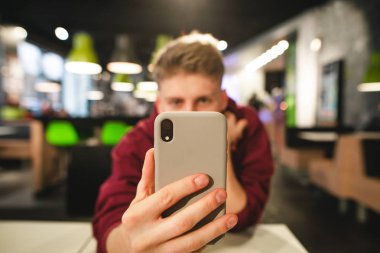 Adam akıllı telefon vasıl onun geçmiş elinde tutuyor. Pozitif genç adam bir fotoğraf bir smartphone bir fast-food Restoran, odak yakın çekim ön planda bir smartphone içinde alır. Boşaltmak