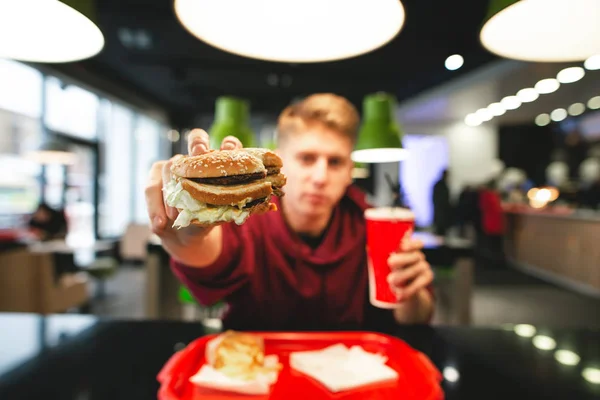 一个微笑着的人手里拿着美味的汉堡 现代年轻人在餐厅吃快餐 向镜头展示美味的开胃汉堡 微笑着 — 图库照片