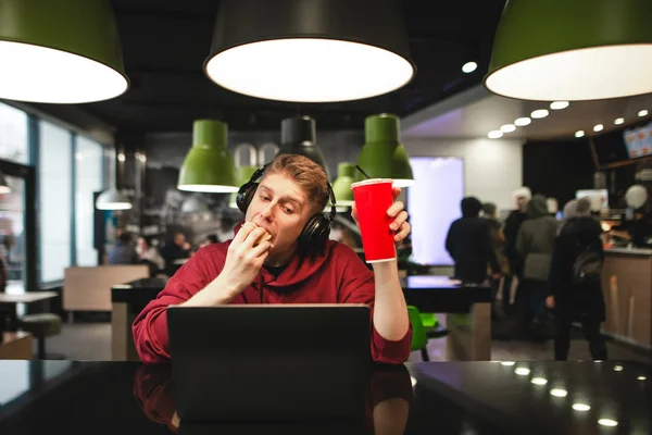 Tipo Los Auriculares Sienta Cafetería Mesa Come Una Hamburguesa Trabaja — Foto de Stock