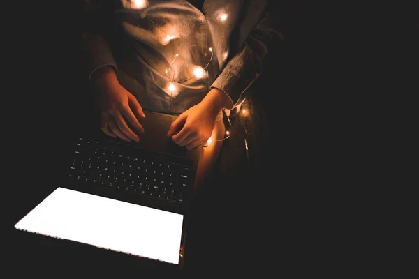 Sexy woman in panties and lights, lying in a bed with a laptop on her legs, top view. Woman works on a laptop with a white screen at night, a dark background. Copyspace