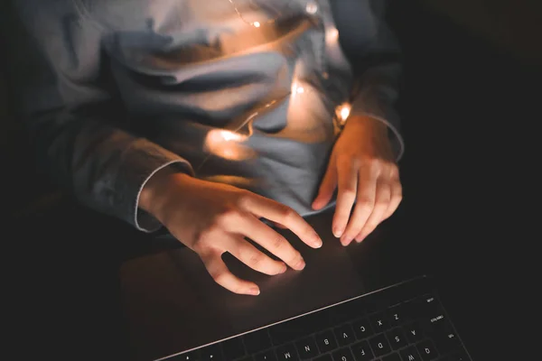Woman using a laptop at night in bed, top view, hands close up. Womens hands, fingers on the touchpad of the laptop. Laptop, gadget, hands, close up.