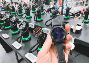 Elektronik dükkandaki adam akıllı bir saat elinde tutar. Bir ışık Teknoloji Mağazası akıllı saat satın. Yakın, el ve akıllı raflar saatler ile arka plan dikkat et.