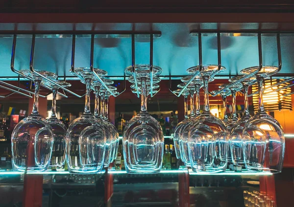 Close photo of glasses in the bar. Crystal clear with blue light on the background of the shelves with the allegor. Glasses hang on a bar with a blue light. Bar, restaurant background.