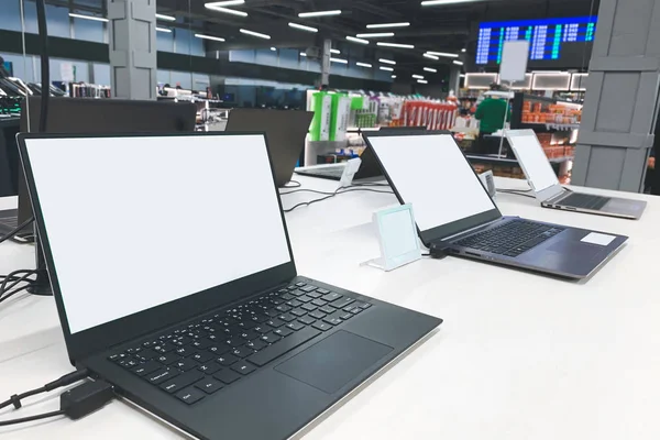 Laptops with a white screen at the showcase in the electronics store. Buy a laptop in a technology store.