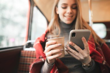Mutlu kız bir akıllı telefon kullanan ve rahat bir kafede kahve içiyor. Yakın çekim bir smartphone ve bir fincan kahve ellerinde. Arka plan. Boşaltmak