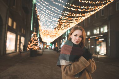 Güzel kız sıcak giysiler içinde ışıklar ile sokakta duruyor 