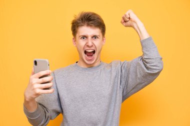 Duygusal çekici bir adam akıllı telefon elinde tutar, kameraya bakıp sevinir. Genç adam onun elinde bir akıllı telefon ile sarı bir arka plan üzerinde izole başarısında sevinir. Boşaltmak