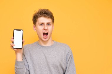 Sürpriz çocuk sarı bir arka plan üzerinde beyaz bir ekran ile bir akıllı telefon tutar ve kameraya doğru görünüyor. Sarı bir arka plan üzerinde izole elinde bir akıllı telefon ile şaşırmış genç adam. Boşaltmak
