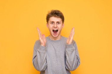 Heyecanlı bir genç adam portresi sarı bir arka plan üzerinde ellerini yukarı kaldırarak hayran bakışla kameraya benziyor. Şaşırmış adam sarı bir arka plan üzerinde izole.