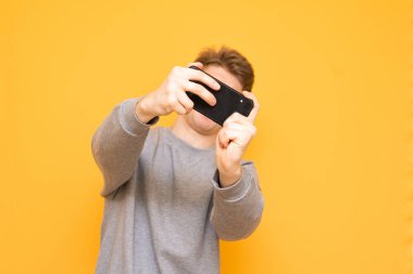 Adam bir smartphone cep telefonu ile sarı bir arka plan üzerinde izole, bir oyun oynuyor. Belgili tanımlık smartphone üzerinde odaklanın. Mobil oyun kavramı.