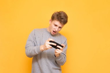 Konsantre adam sarı bir arka plan üzerinde ve Smartphone'da oyunlar oynuyor. Mobil oyun. Bir smartphone oyun oyun oyunlar. Boşaltmak