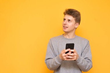 Casual giyim olumlu genç bir adam portresi onun elinde, gülümser bir akıllı telefon ile duruyor ve yanlara sarı bir arka plan üzerinde görünüyor. Boşaltmak