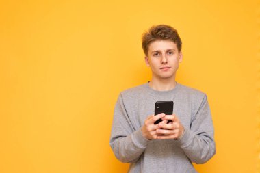 Casual giyim, güzel bir adam portresi smartphone elinde gülümsüyor tutar ve sarı bir arka plan üzerinde izole kameraya benziyor. Sarı arka plan üzerinde elinde telefon ile genç adam