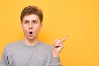 Yakın çekim görünüyor bir adam portresi kameraya şaşırttı ve sarı bir arka plan üzerinde izole boşaltmak, bir parmak gösterir.