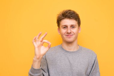 Sarı bir arka plan üzerinde mutlu adam Tamam tabelaya gülümsüyor. Genç adam gösterir ne seviyor, sarı bir arka plan üzerinde izole kamera bakar. Boşaltmak
